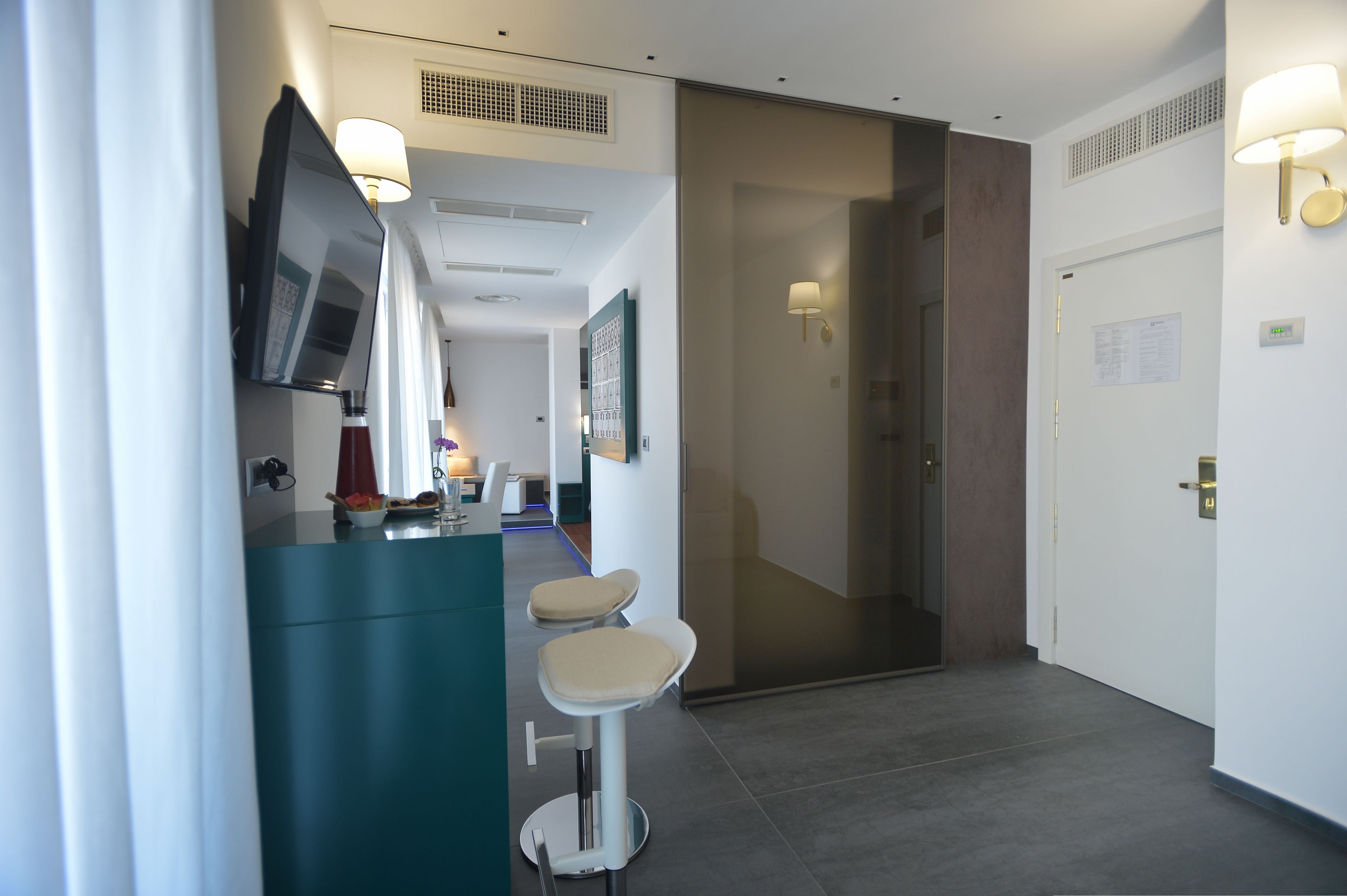 Un couloir d’hôtel moderne avec un espace bar, des sièges et une porte donnant accès à une chambre.
