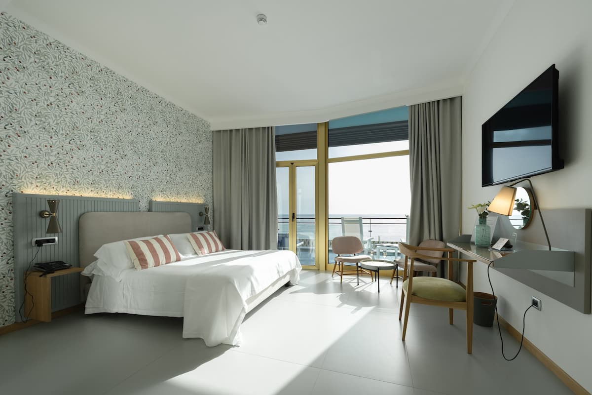 Ein modernes Hotelzimmer mit einem großen Bett, einem Schreibtisch mit Stuhl, einem Fernseher und einem Balkon mit Blick.