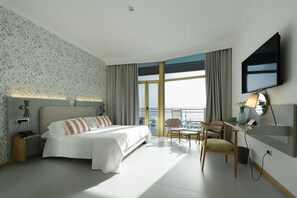 Habitación de hotel moderna con una cama grande, un escritorio con silla, televisión y balcón con vistas.