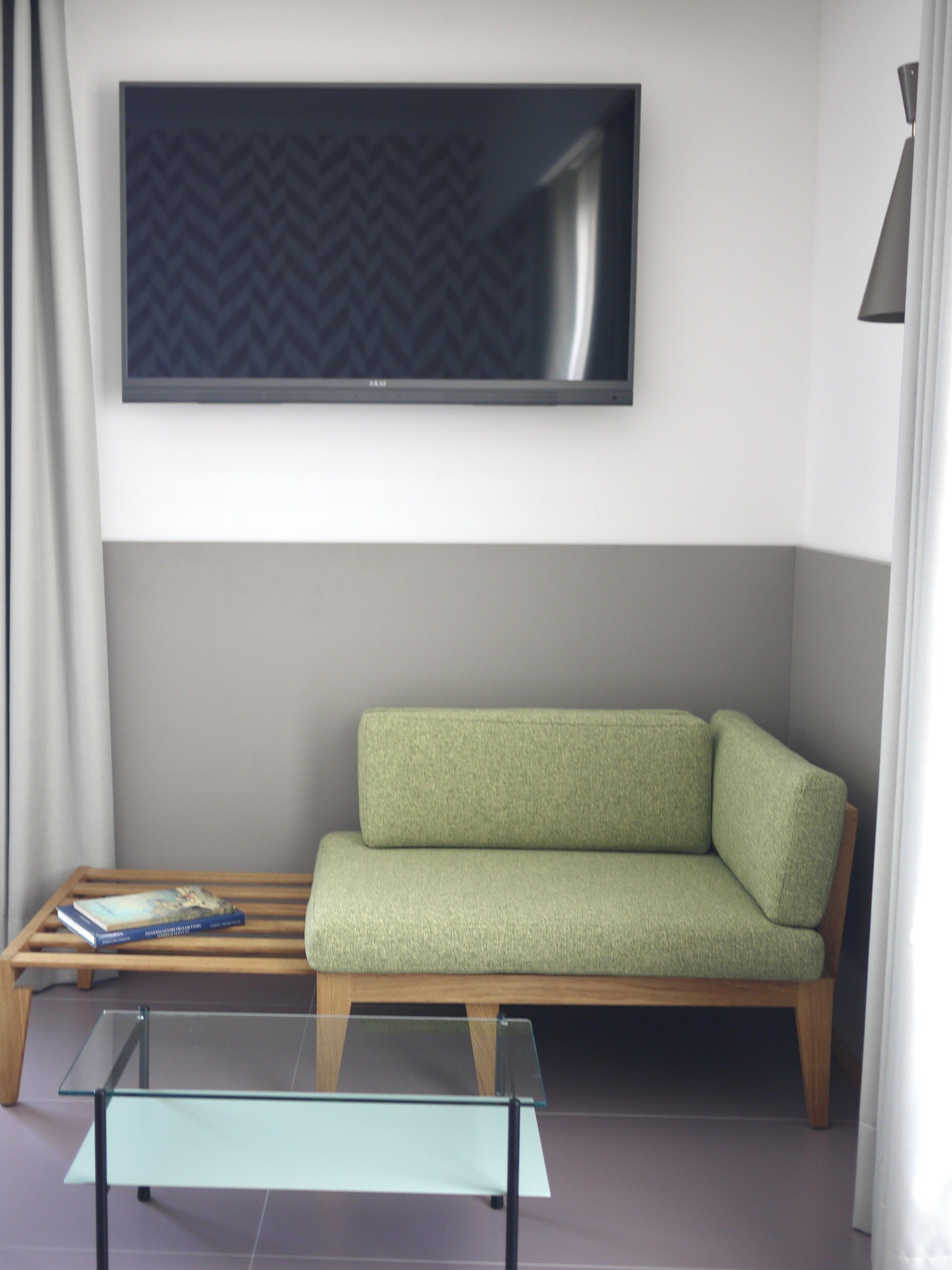 A modern living room with a green sofa, a glass coffee table, and a flat-screen TV mounted on the wall.