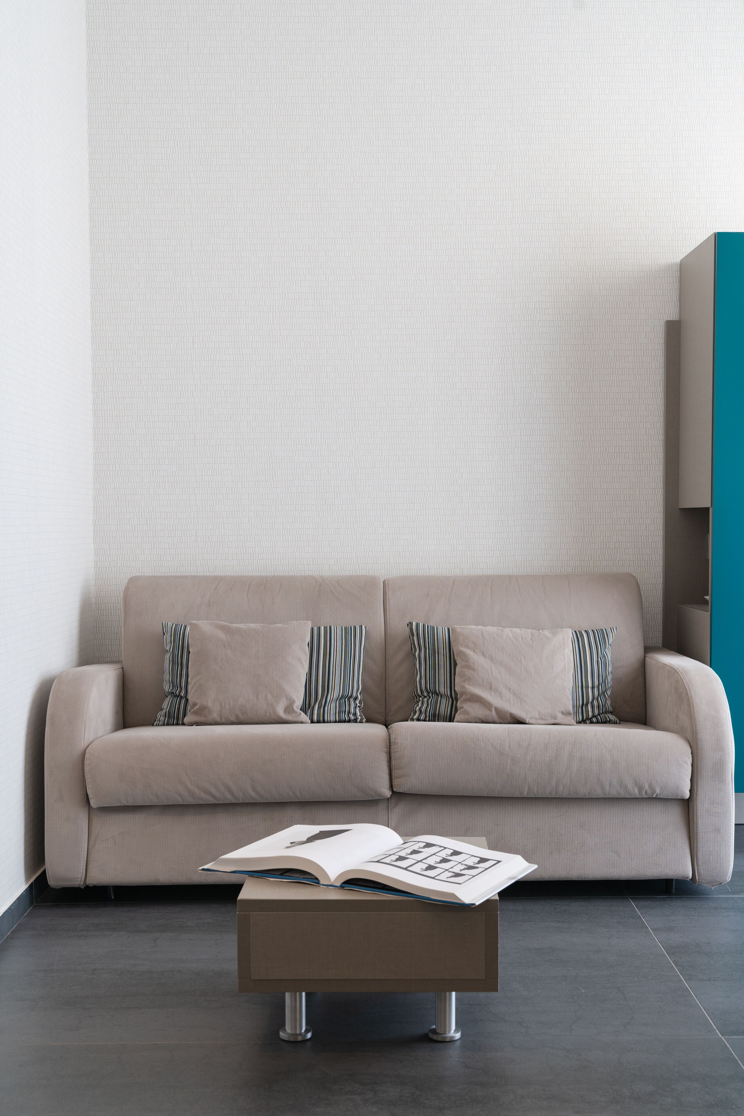 A beige sofa with striped pillows against a textured wall, a wooden coffee table with a book, and a dark floor.
