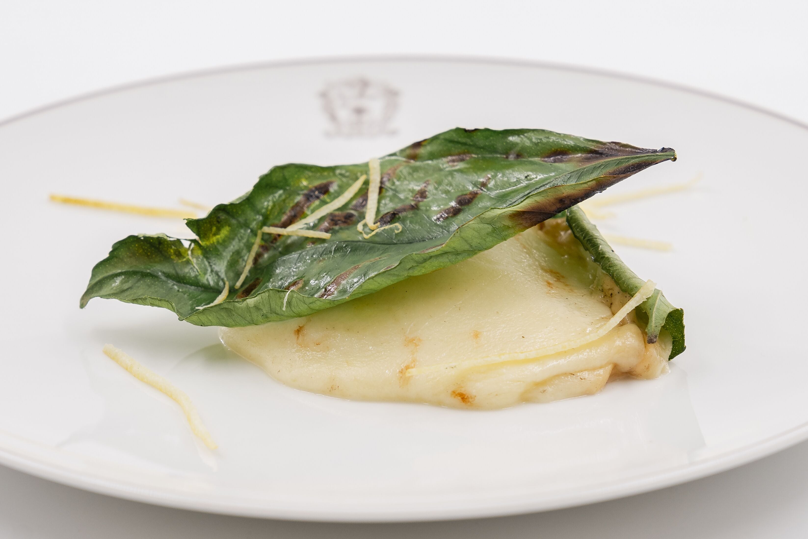 Un plato con un alimento, posiblemente un plato de queso, adornado con una hoja y tiras finas de un vegetal amarillo.