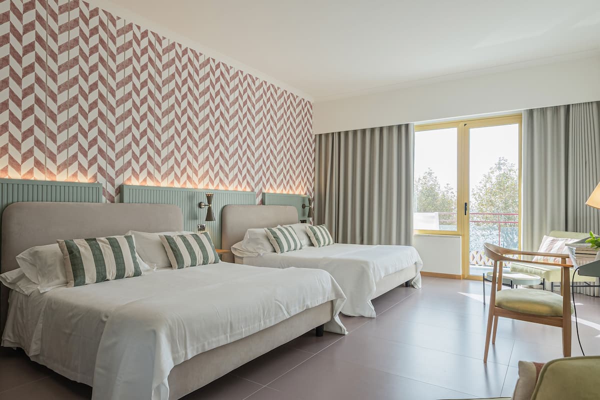 Ein Hotelzimmer mit zwei Betten, einem großen Fenster mit Vorhängen, einem kleinen Tisch und einem Stuhl.