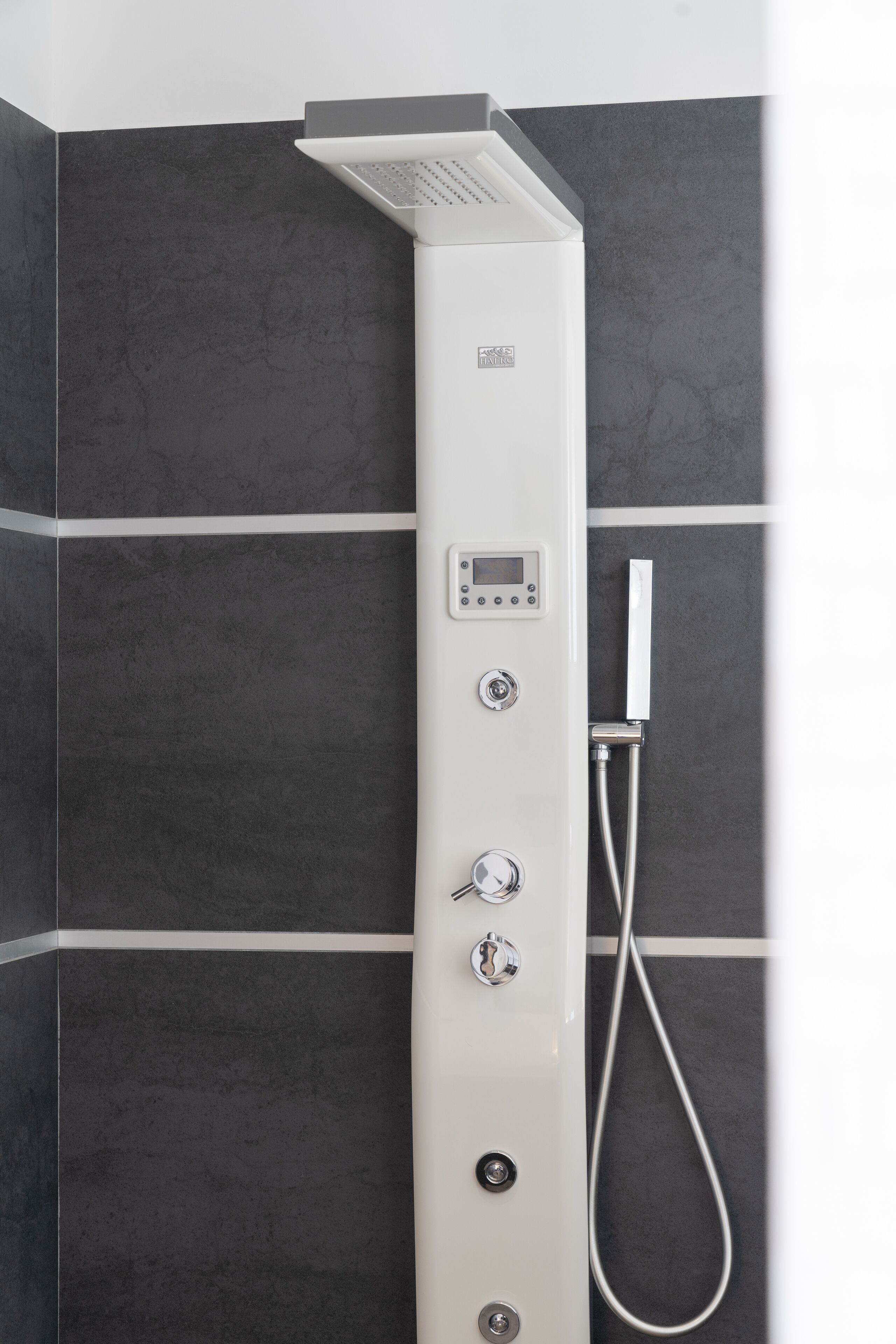 A modern shower with a control panel and a handheld showerhead against a tiled wall.