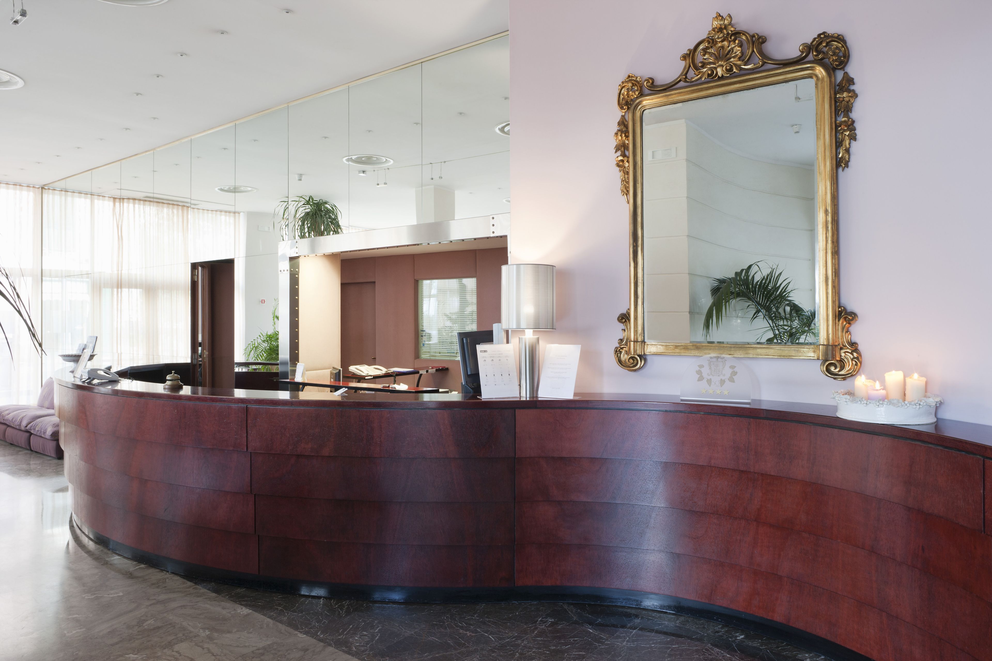 Un área de recepción con un mostrador de madera curvada, un espejo grande y una zona de estar con un sofá y una silla.