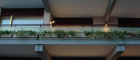Een hotel met meerdere balkons, versierd met planten, grote ramen en een goed verlichte entree.
