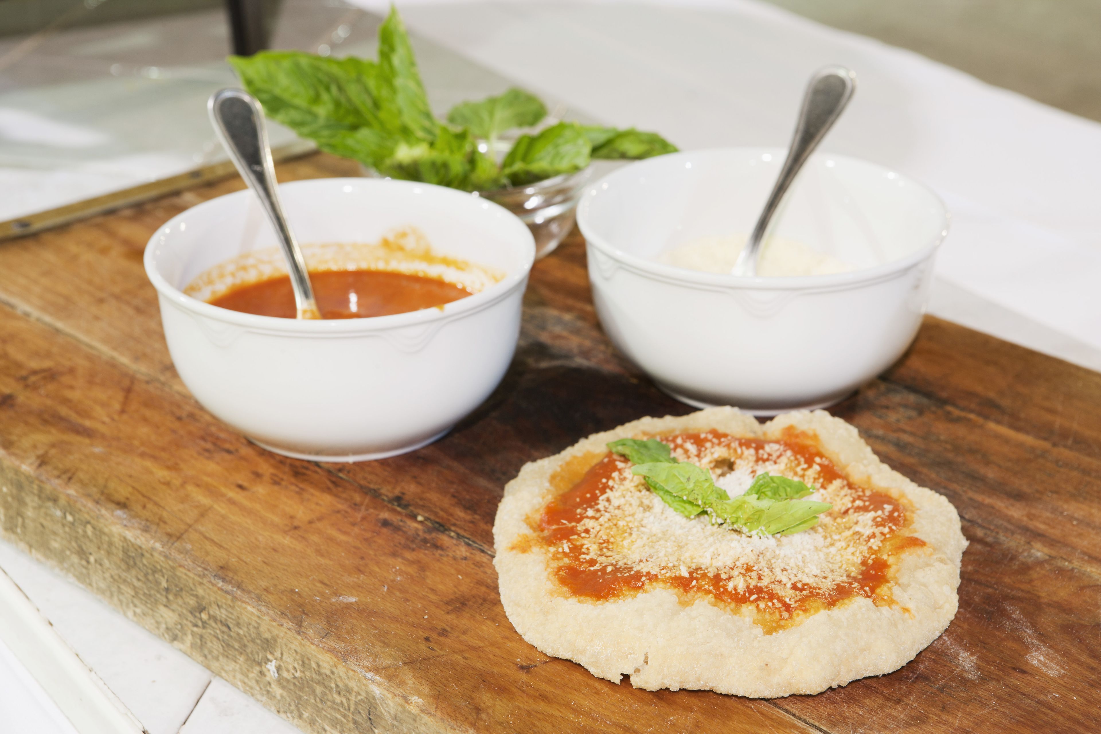 A wooden board with two bowls of sauce and a small bowl of cheese.