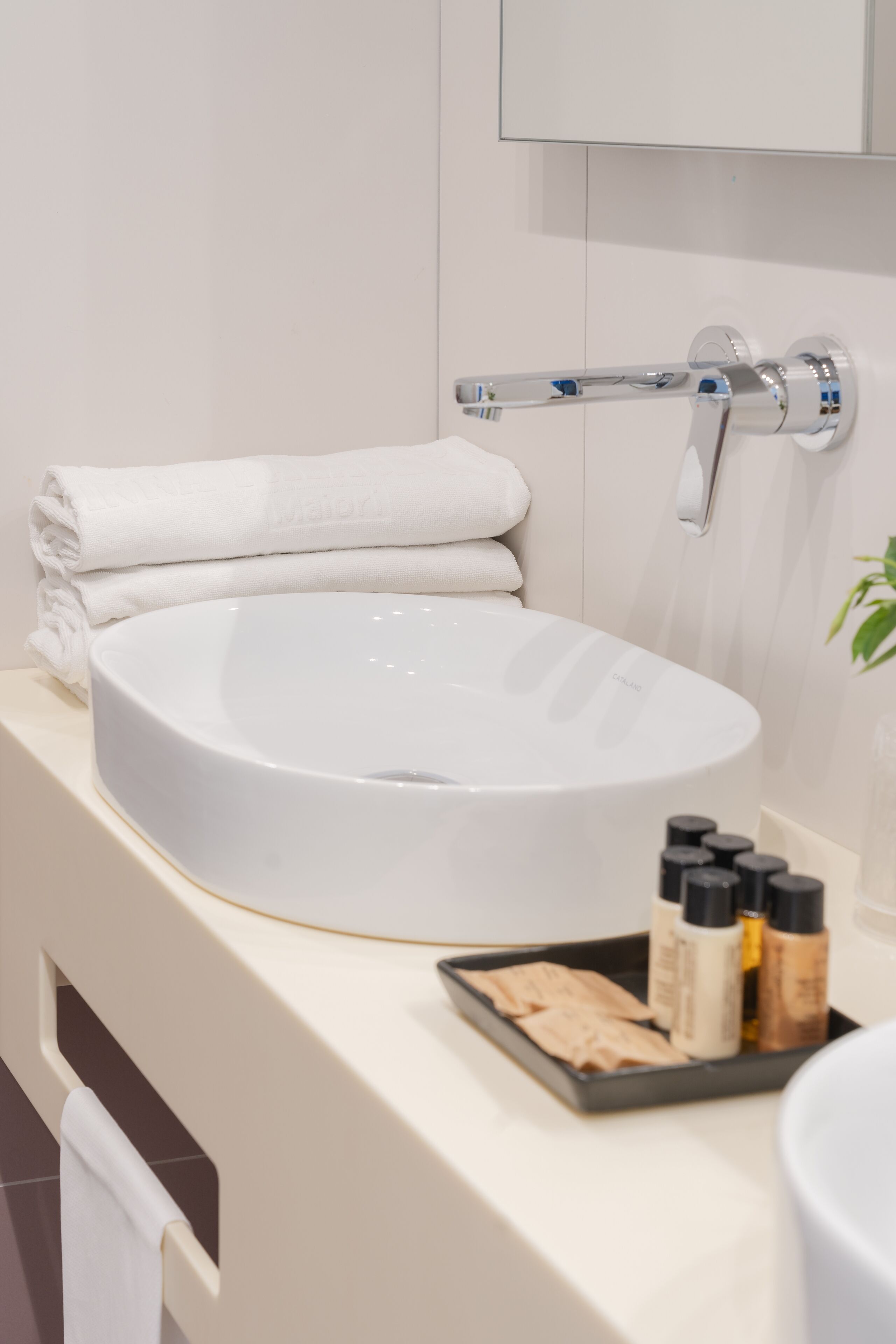 A modern bathroom with a large, round white sink, a towel rack with folded towels, and a tray with toiletries.