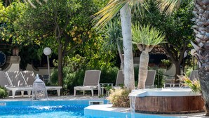 Una piscina con una fuente de agua, rodeada de palmeras y sillas de descanso.