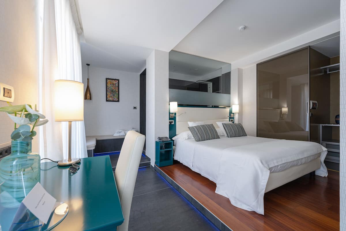 Ein modernes Hotelzimmer mit Bett, Schreibtisch, Stuhl und einem großen Spiegel.