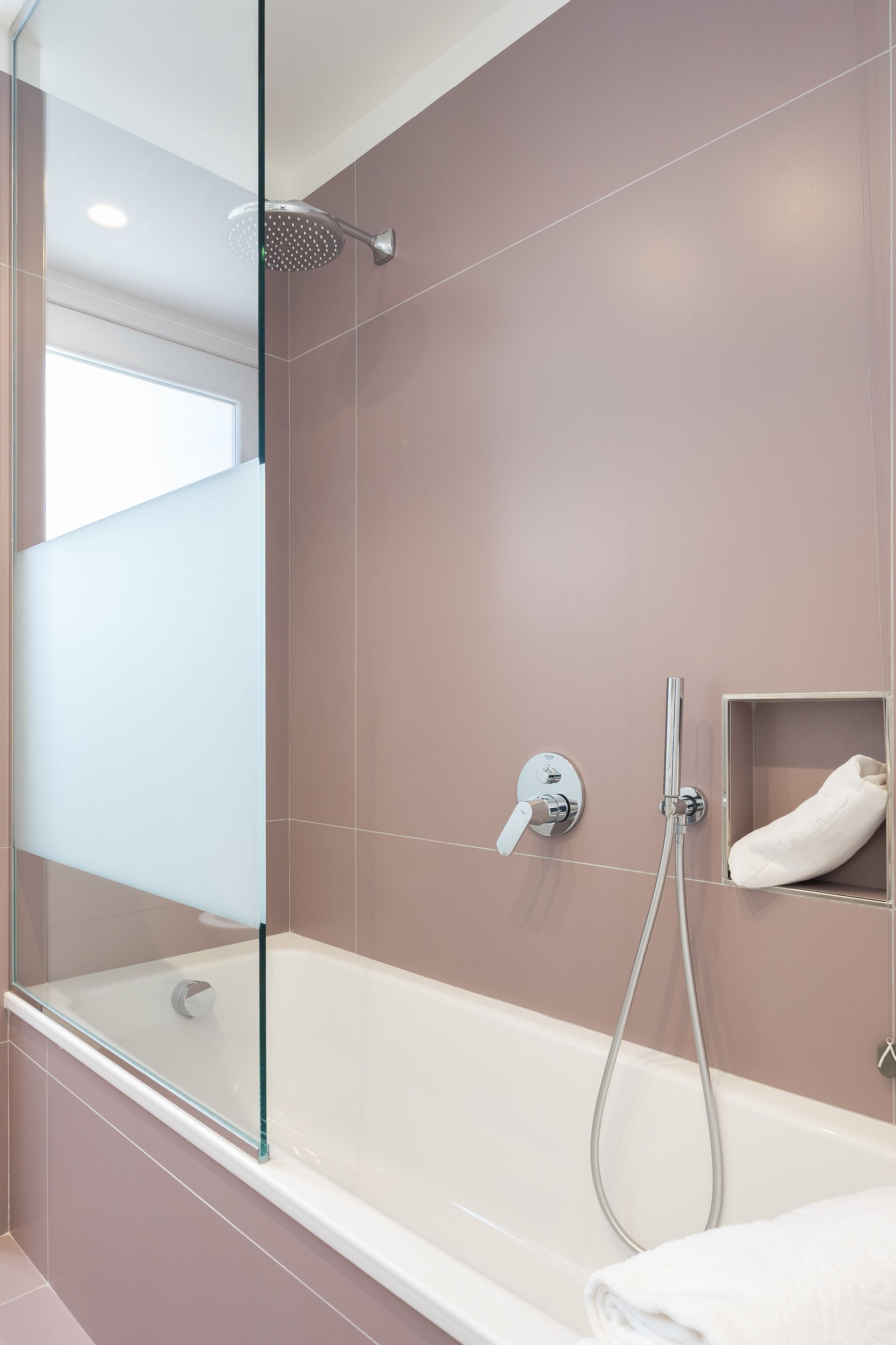 A modern bathroom with a glass-enclosed shower, a white bathtub, and a towel shelf.