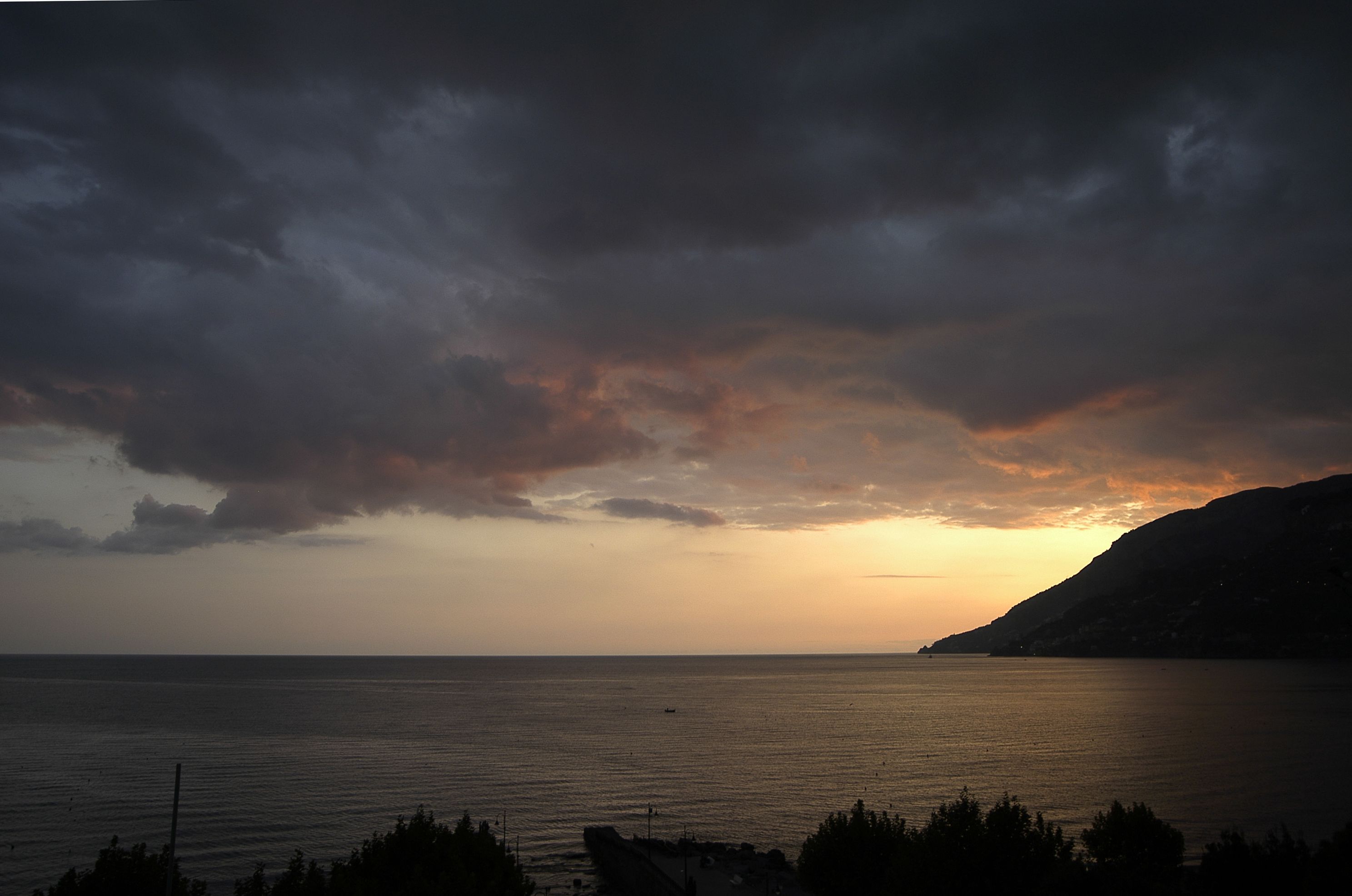 Un paisaje costero con un atardecer sobre el mar, la silueta de una colina y un cielo despejado.