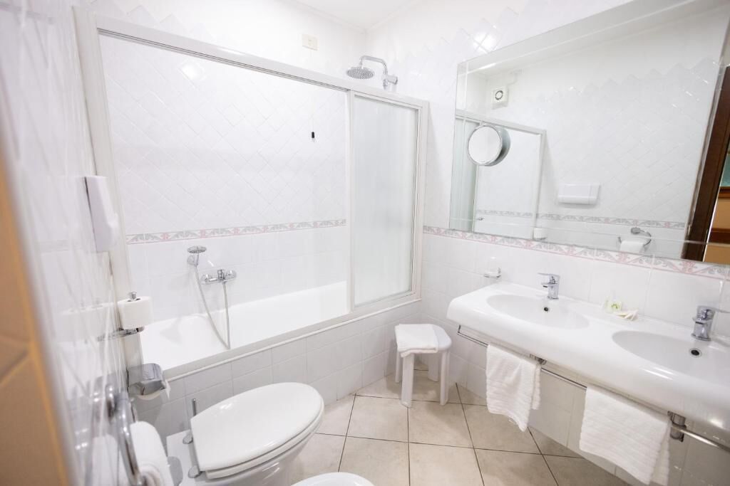 A bathroom with a toilet, a sink, a shower, and a mirror.