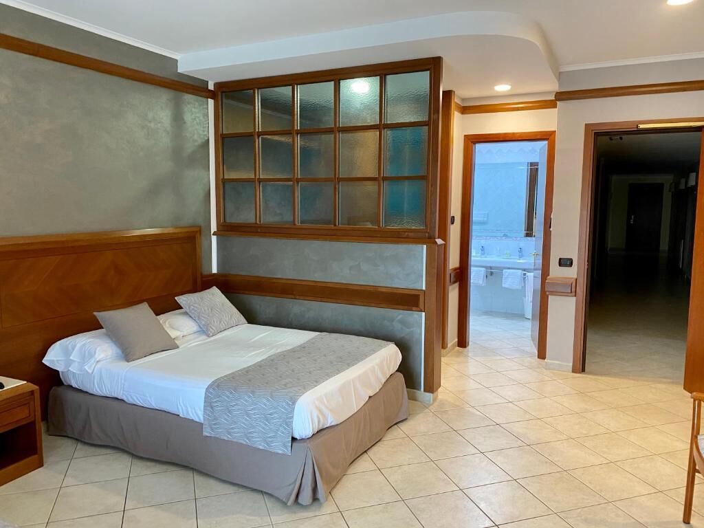 A bedroom with a large bed, wooden headboard, and a view through a glass partition.