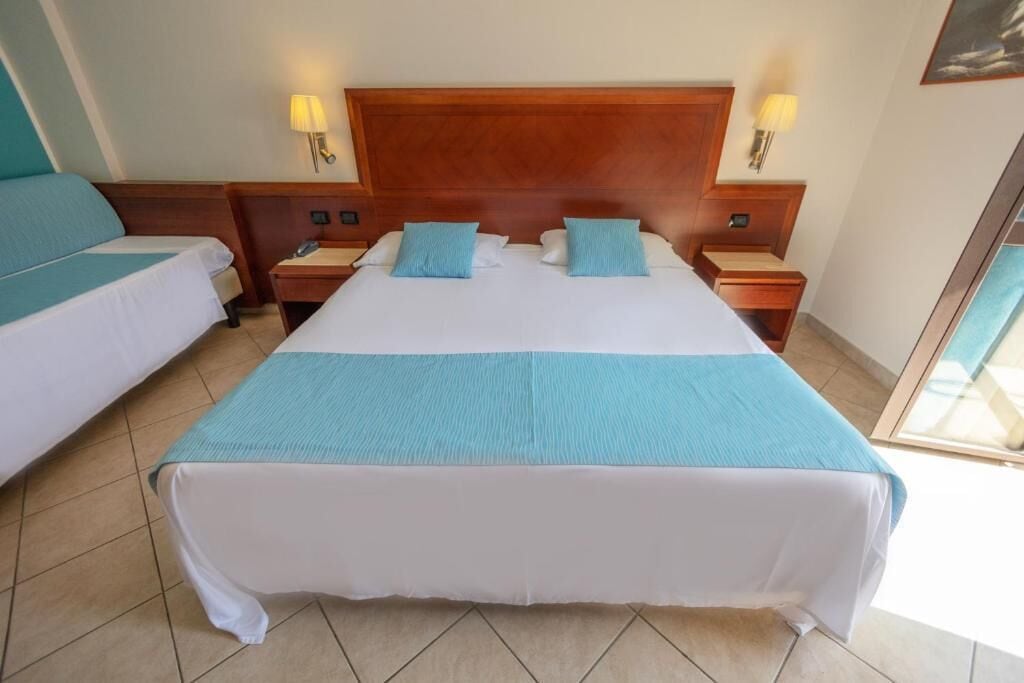 A hotel room with a large bed, two bedside tables, and two lamps.