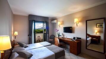 A hotel room with two beds, a desk, a chair, a TV, and a balcony with a view.
