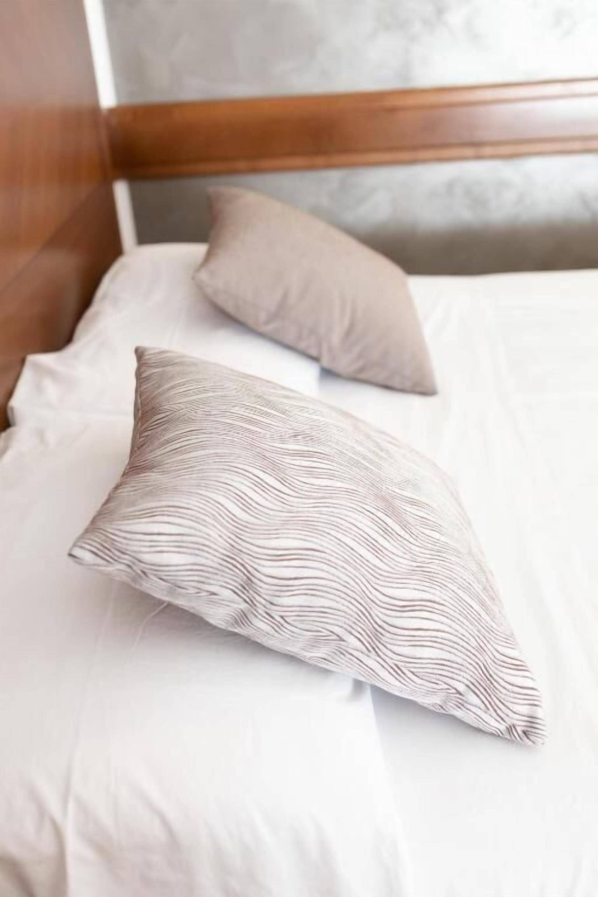 Una cama con ropa de cama blanca y dos almohadas, una con estampado a rayas y la otra lisa.