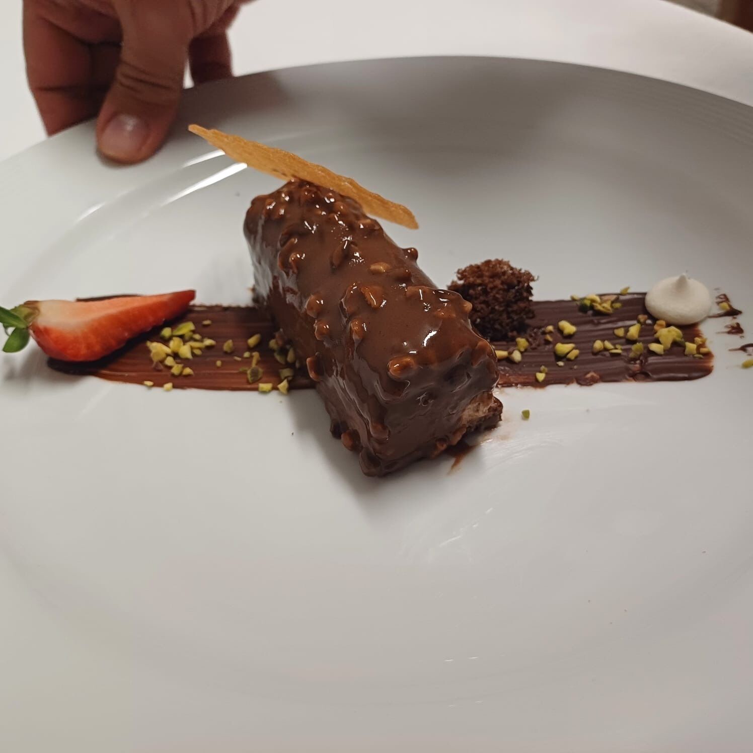 Un dessert su un piatto bianco con glassa al cioccolato, una fragola e noci sparse.