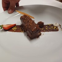 Un postre sobre un plato blanco con cobertura de chocolate, una fresa y nueces esparcidas.