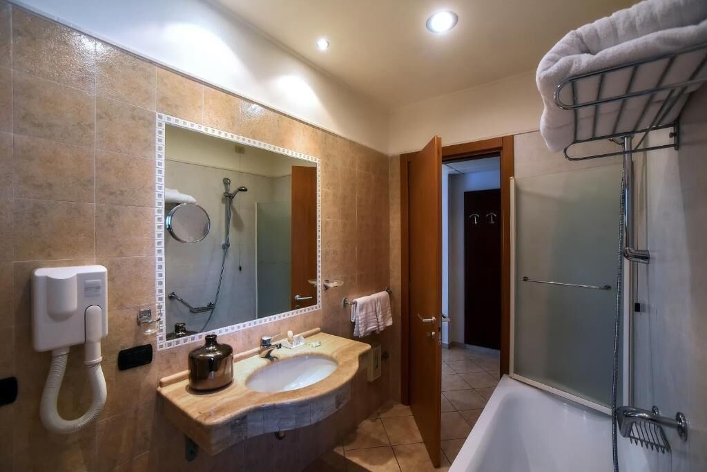 Casa de banho com lavatório, espelho, chuveiro e porta-toalhas.
