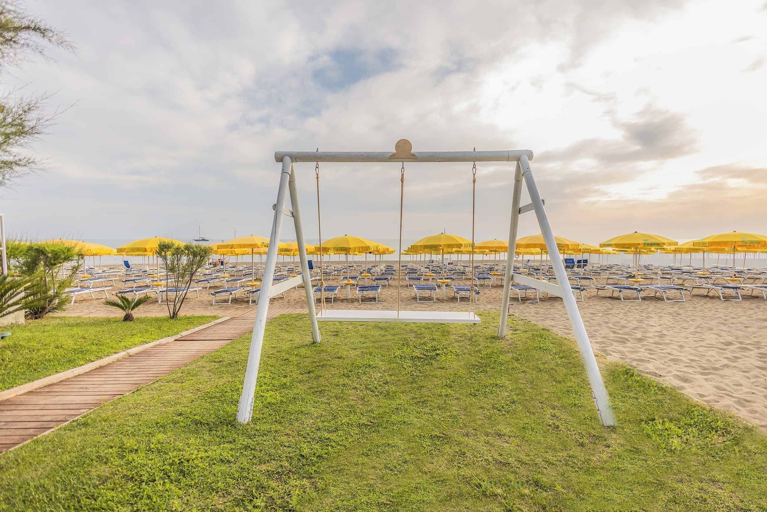 Une plage avec des balançoires, des rangées de transats et des parasols jaunes.