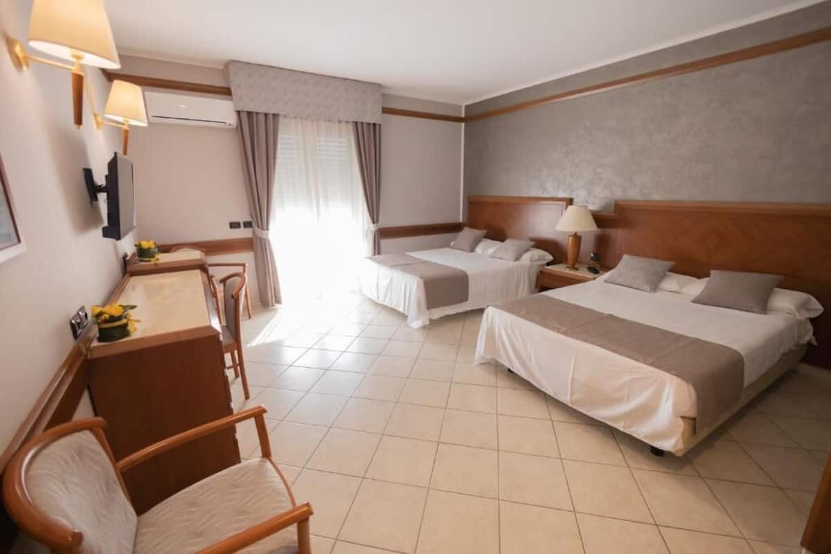 A hotel room with two beds, a desk with a chair, a TV, and a window with curtains.