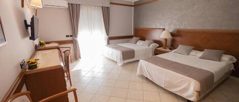 A hotel room with two beds, a desk with a chair, a TV, and a window with curtains.