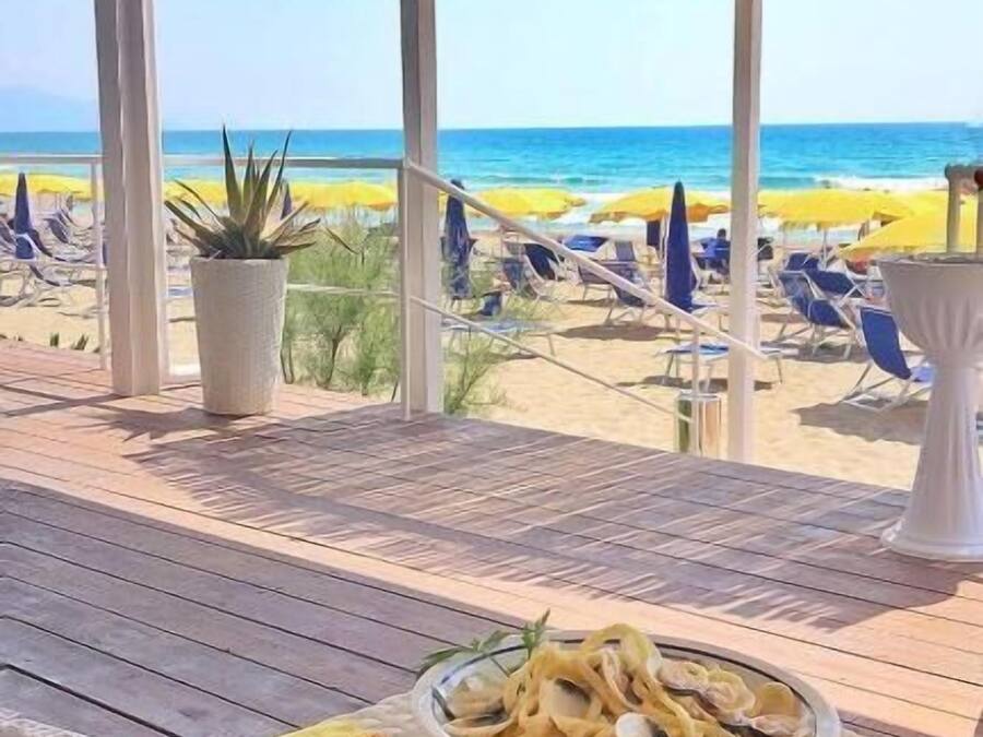 A beachside dining area with a view of the ocean, featuring a pergola and lounge chairs.