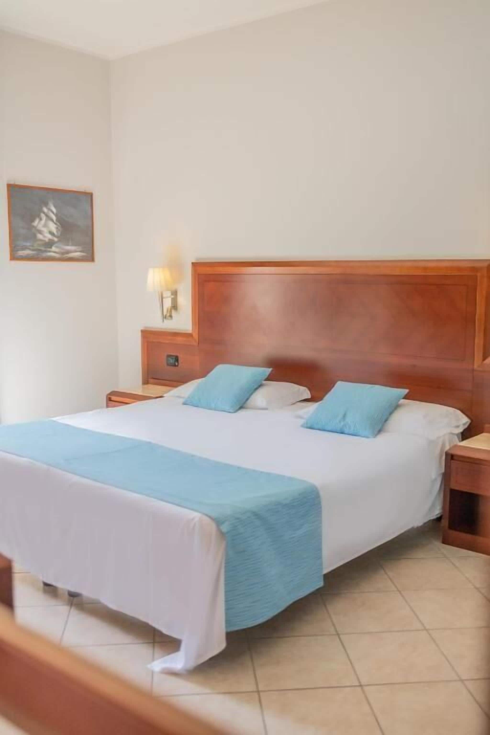 Una camera d'albergo con un letto grande, una testiera in legno, due comodini con lampade e un quadro appeso al muro.