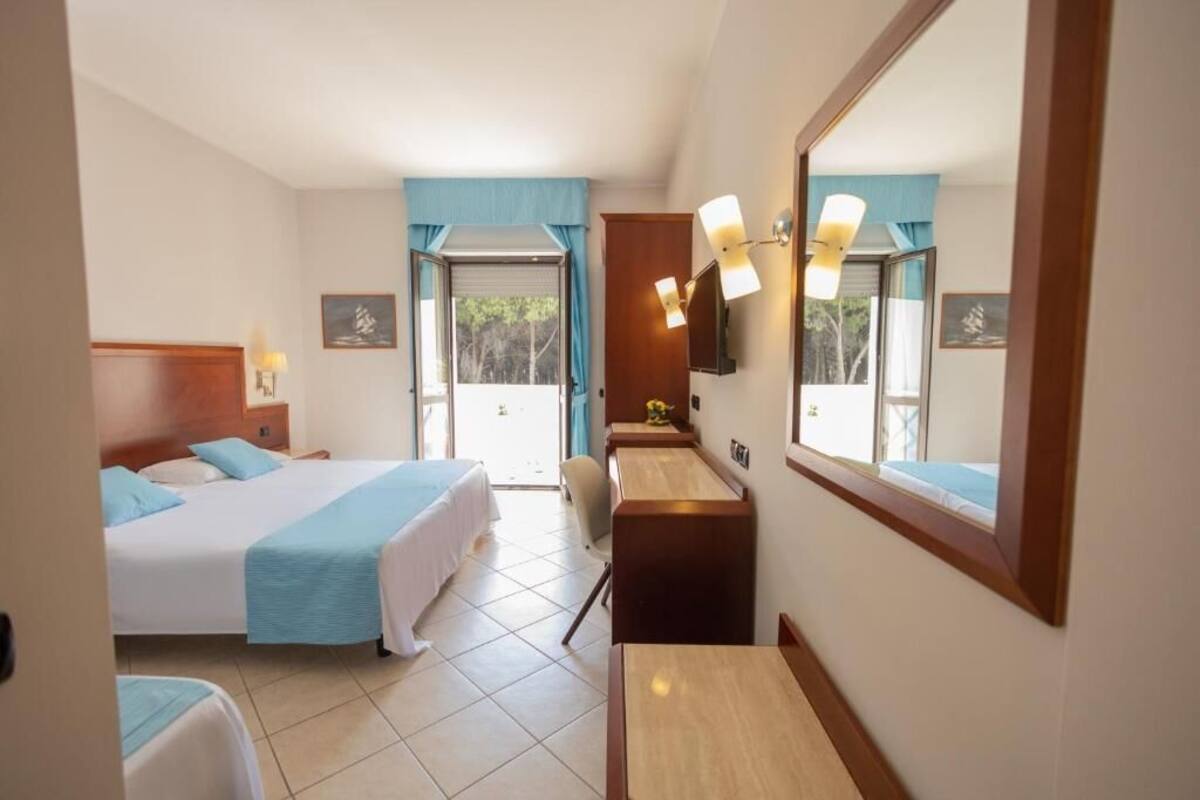 A hotel room with a bed, a desk, a chair, a mirror, and a window with curtains.