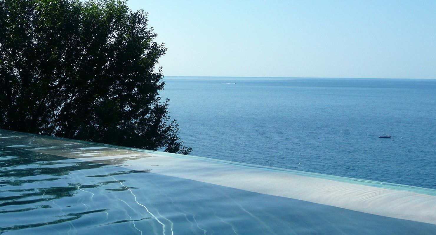 Vista despejada de una playa con piscina y un barco a lo lejos.