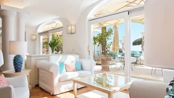Ein großzügiger Wohnbereich mit einem weißen Sofa, einem Glastisch und Blick auf eine Außenpatio mit Sonnenschirmen und Sitzgelegenheiten.