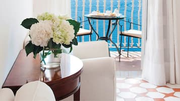 A dining area with a table and chairs, a vase with flowers, and a view of the sea through a balcony.