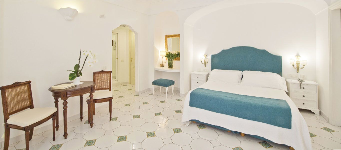 A bedroom with a bed, two bedside tables, a chair, a small table, and a potted plant.