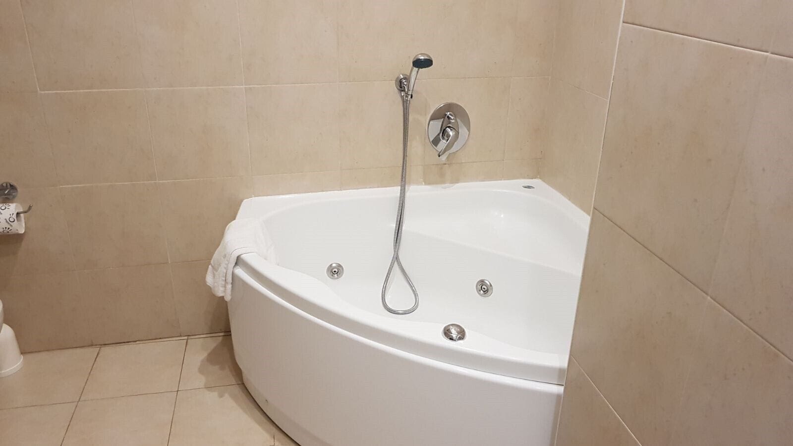 A white bathtub with a handheld showerhead, beige tiled walls, and a white floor.