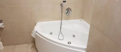 A white bathtub with a handheld showerhead, beige tiled walls, and a white floor.