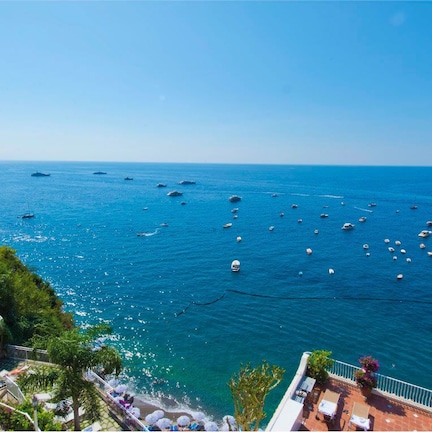 A coastal view with a swimming pool, a large tree, and boats on the water.