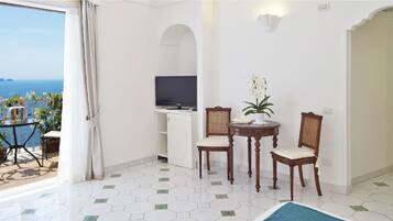 A room with a balcony, a television, a small table with chairs, and a potted plant.