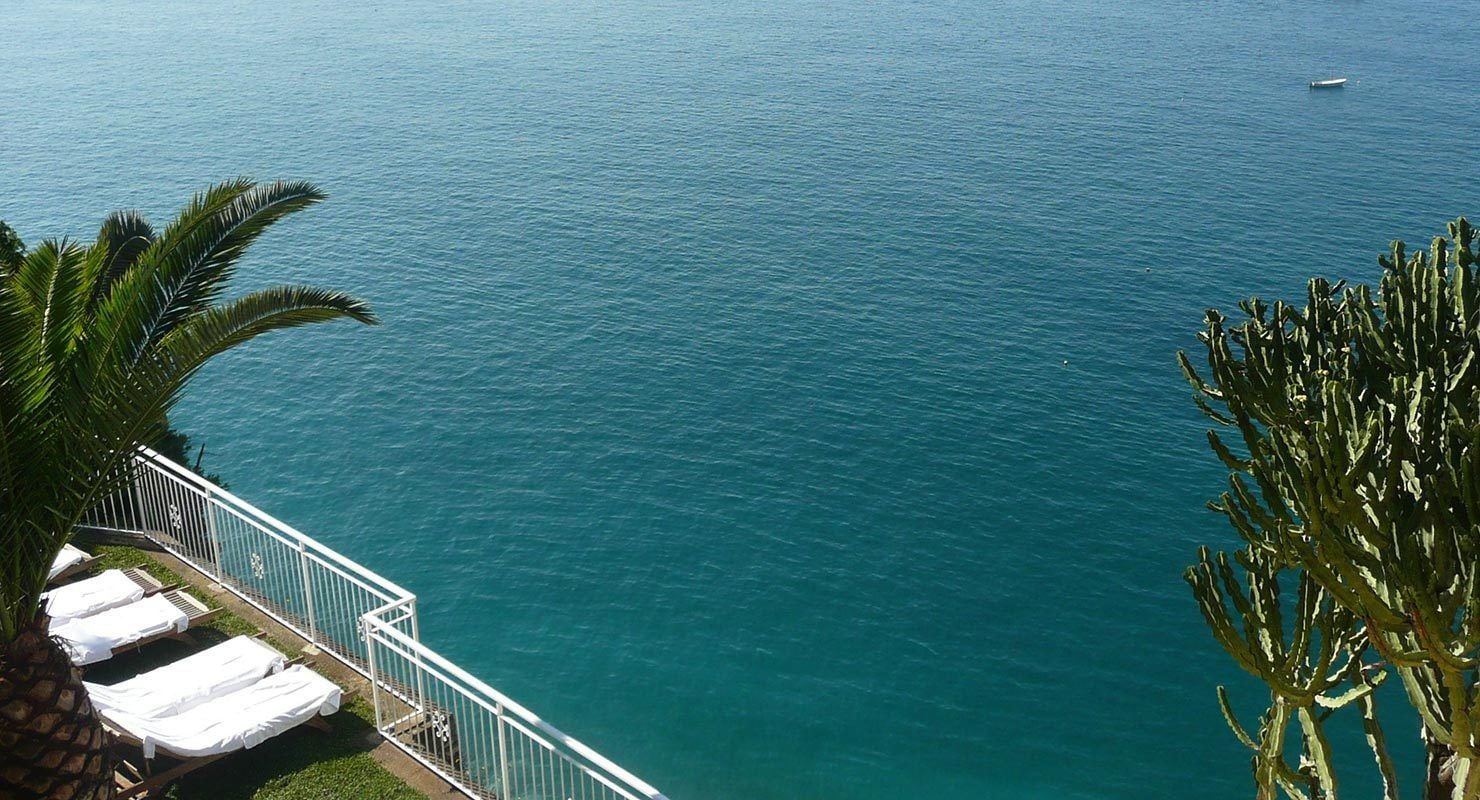 A balcony with white lounge chairs and a railing overlooking a calm sea.