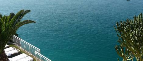 A balcony with white lounge chairs and a railing overlooking a calm sea.