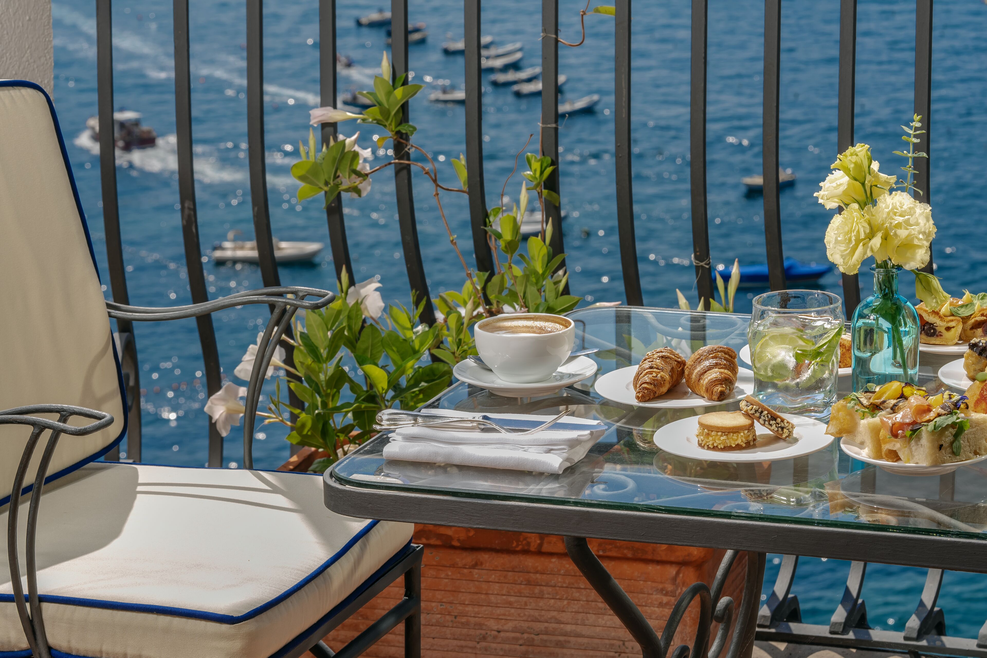 A dining table with plates of food, a cup of coffee, and a glass of water, set against a backdrop of a body of water with boats.