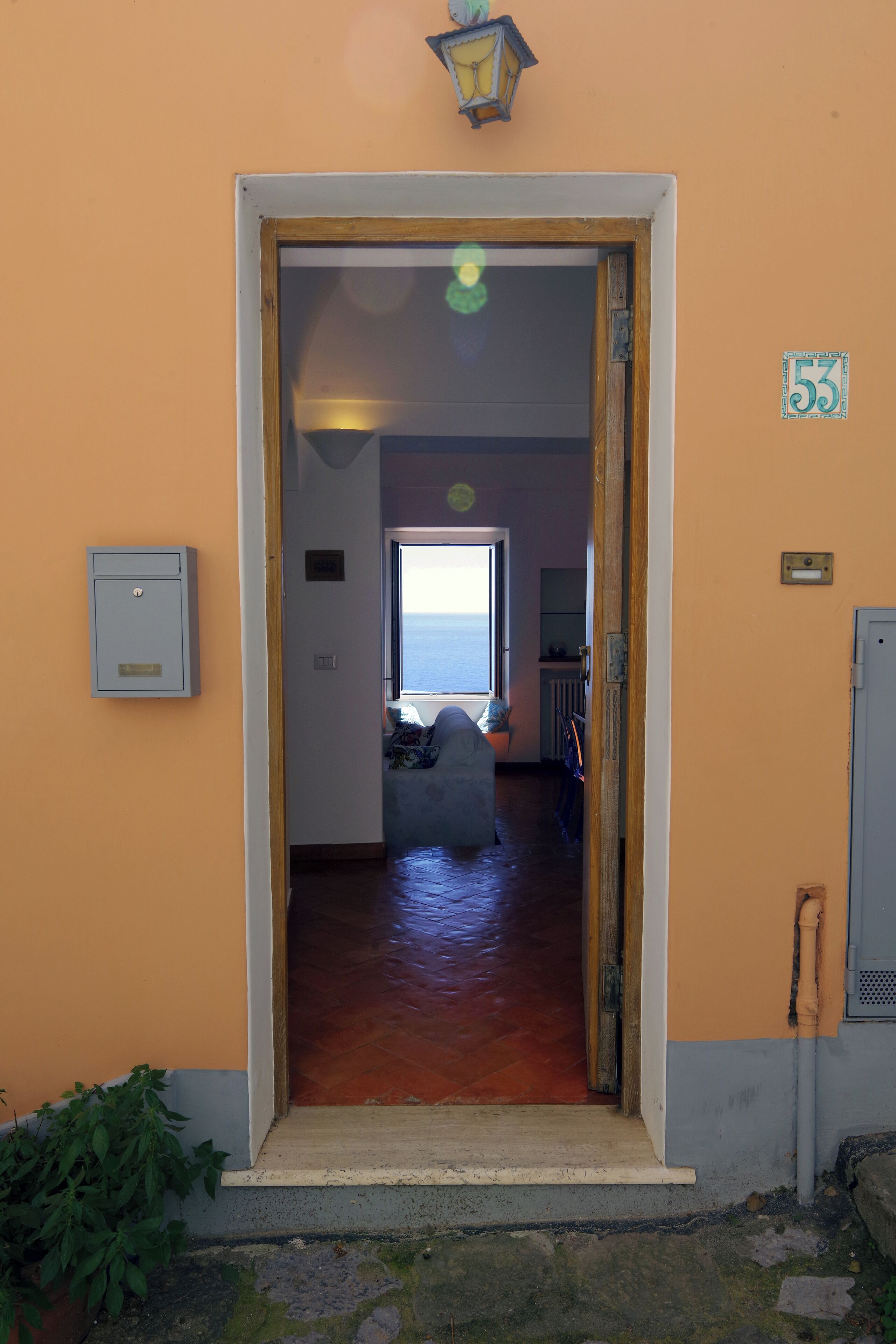 Una puerta que da a una habitación con vistas al mar, una planta en maceta y un letrero con el número 53 en la pared.