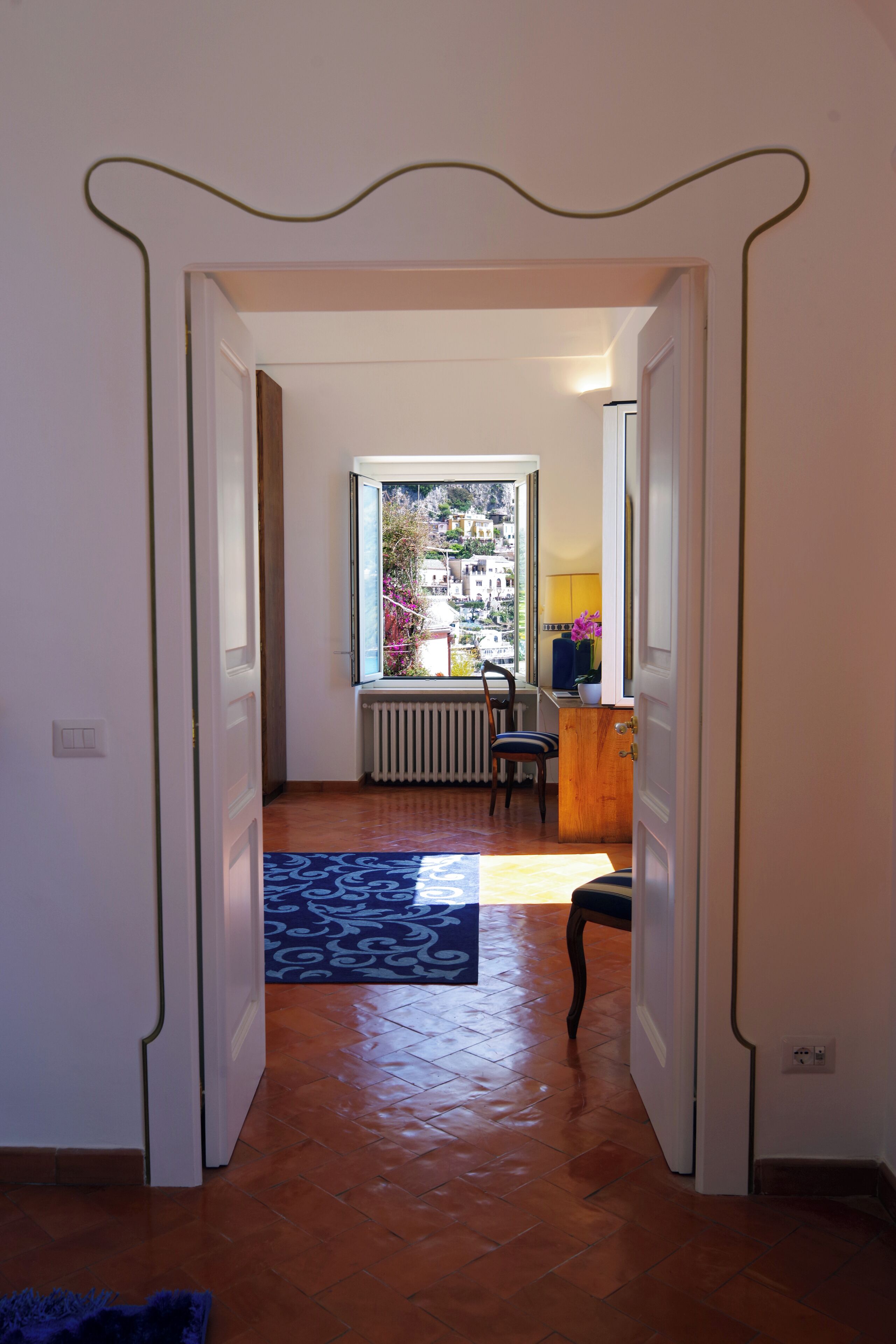 A hallway with a radiator, a chair, and a view of buildings outside.