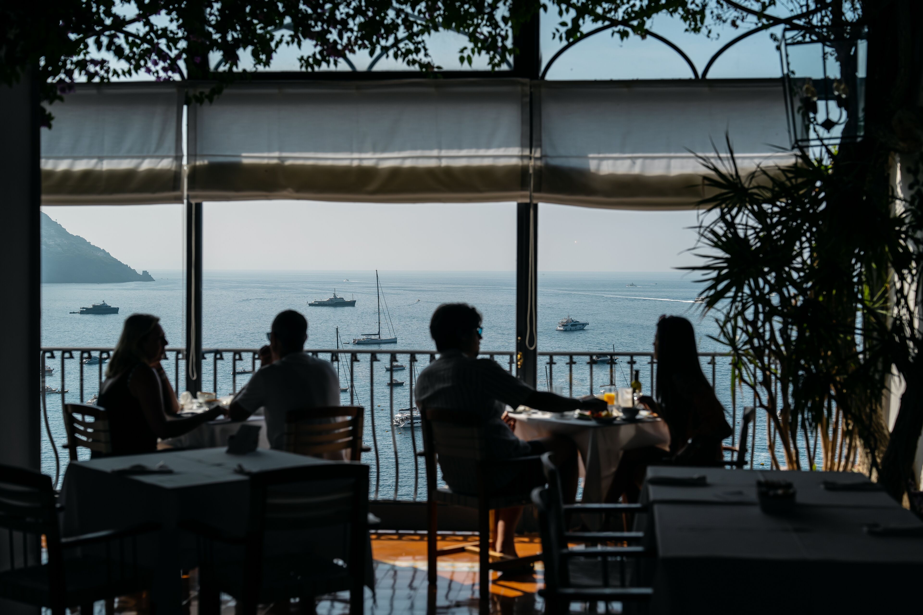 A restaurant with outdoor seating overlooking the sea, featuring tables and chairs arranged for dining.