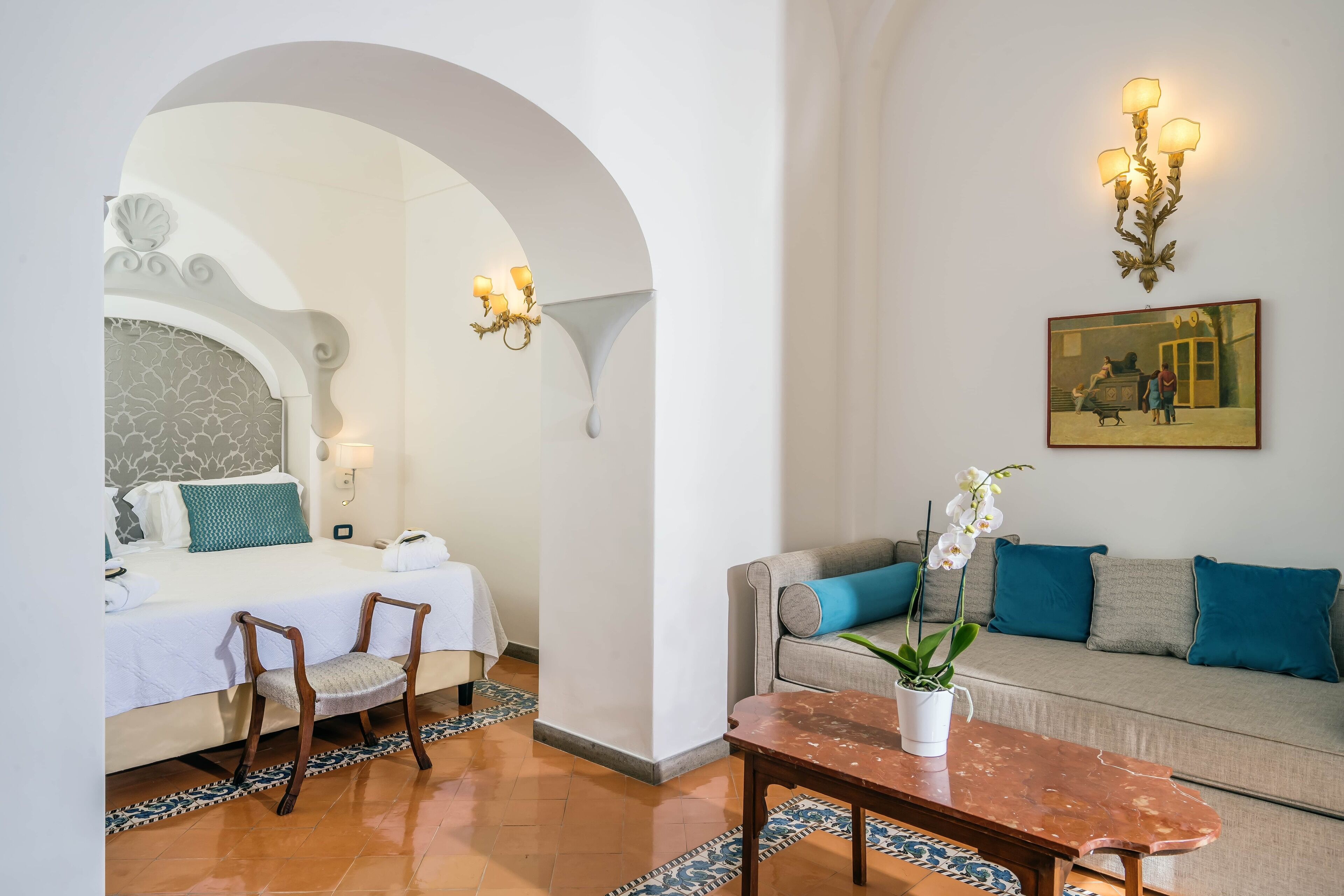 Una habitación de hotel con cama, sofá, mesa de centro y un cuadro en la pared.