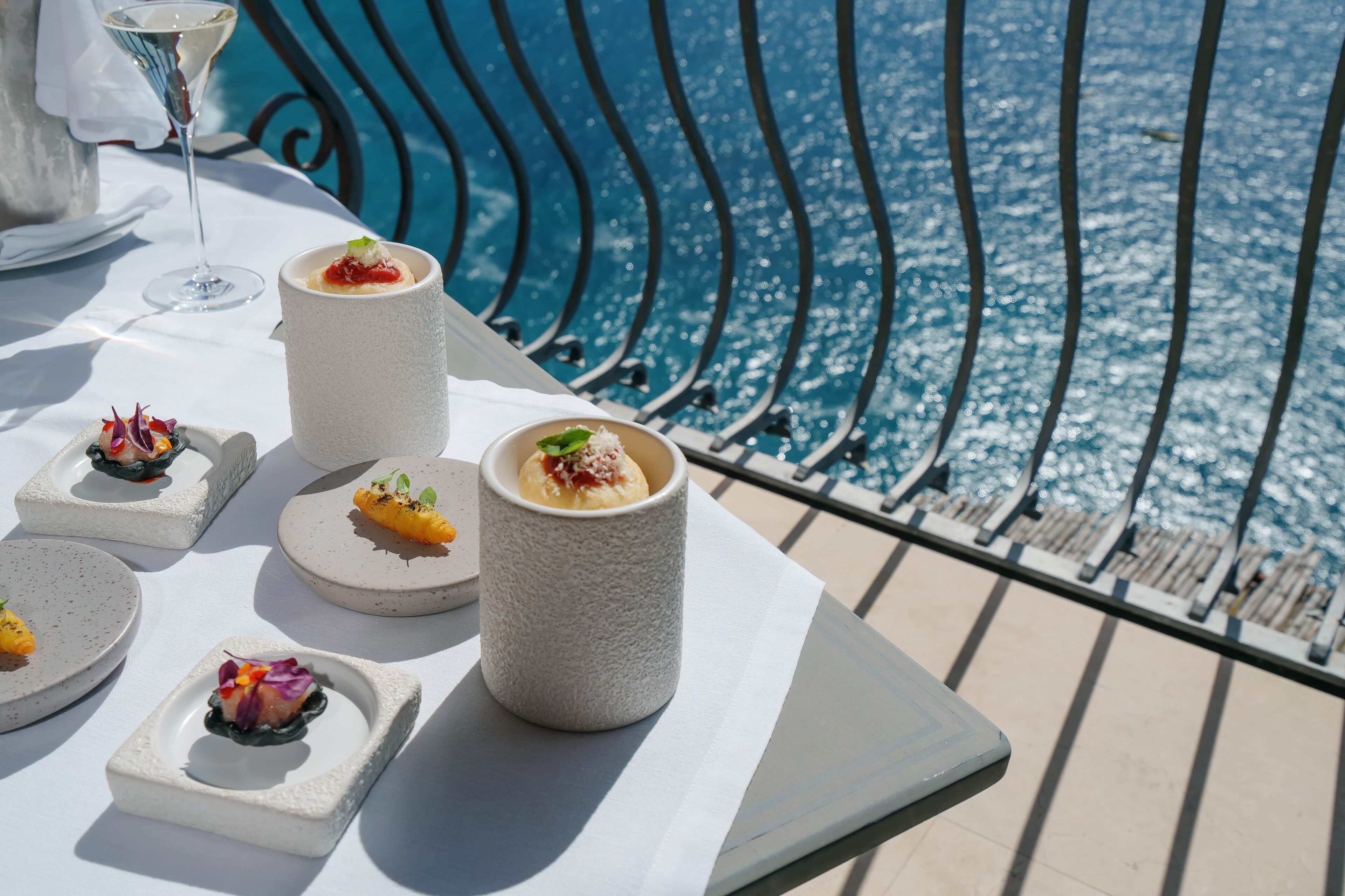 Una mesa con diferentes platos y una copa de vino, con vistas a una piscina.