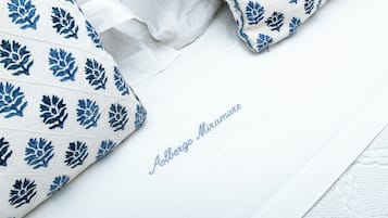 Almofada branca com padrões de folhas azuis e o texto "Alberto Miramonte" sobre uma superfície branca.