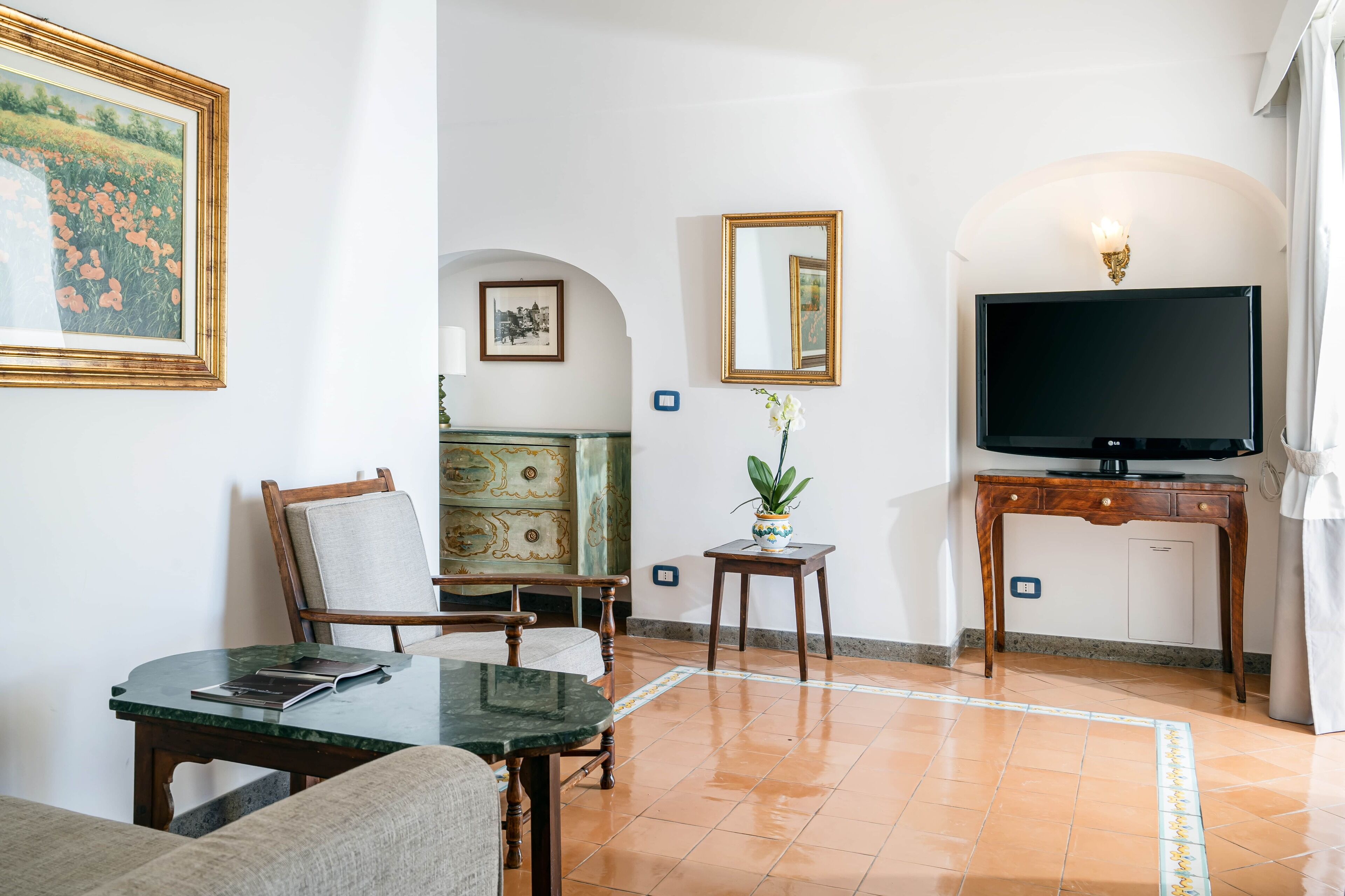 Uma sala de estar com televisão, sofá, mesa de centro, poltrona, pequena mesa com uma planta e um armário.