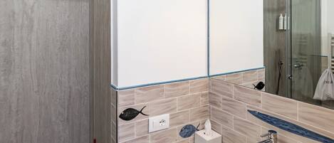 A modern bathroom with a glass shower enclosure, a white sink, and a large mirror with integrated lighting.