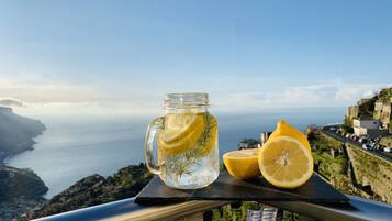 A glass jar with lemon slices and a lemon half on a balcony overlooking a coastal view.